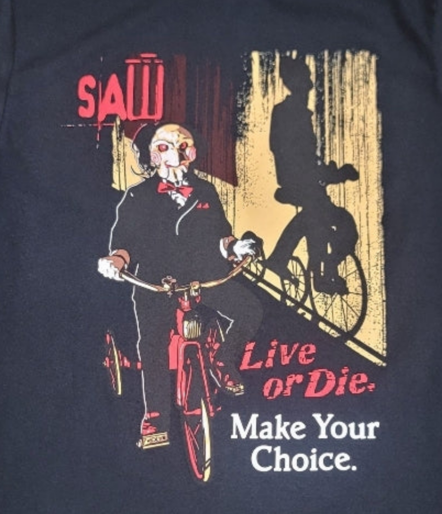 Black Saw t-shirt featuring Billy the Puppet on a tricycle with “Live or Die, Make Your Choice” text – Unisex Silkscreen