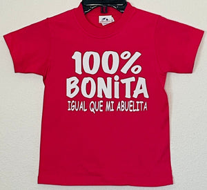 "100% Bonita Cómo Mi Abuelita" Youth Silkscreen T-Shirt in hot pink with bold black text, showcasing a playful and heartwarming design. Displayed flat with a clean background, available in sizes XS-XL. Perfect for kids who love their grandma!                                                                                                    