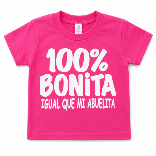 100% Bonita Como Mi Abuelita hot pink infant graphic T-shirt with bold white Spanish family saying, available in sizes 6M-24M.