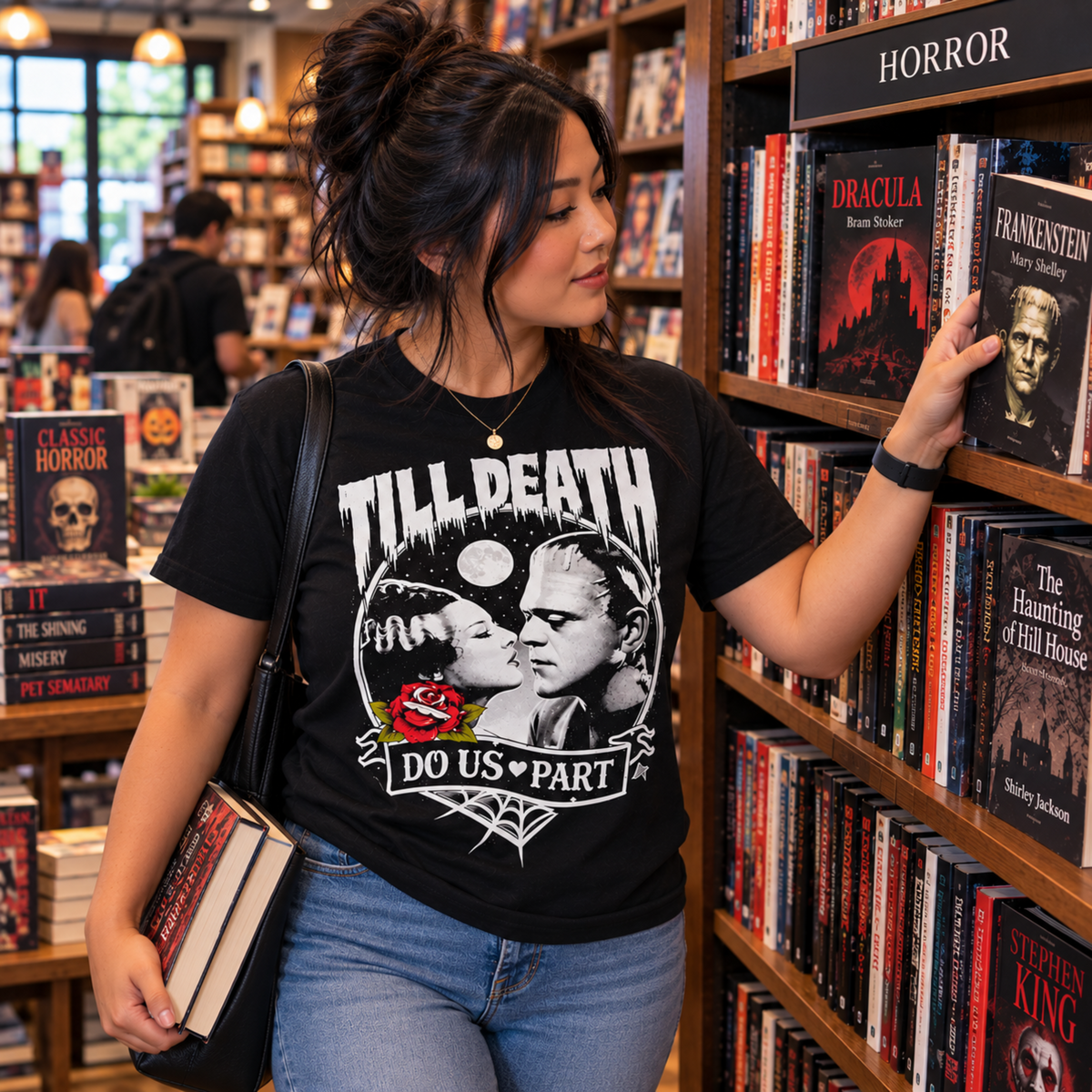 Woman wearing the Till Death Do Us Part black T-shirt while browsing the horror section of a bookstore, featuring Bride of Frankenstein and Frankenstein’s monster.