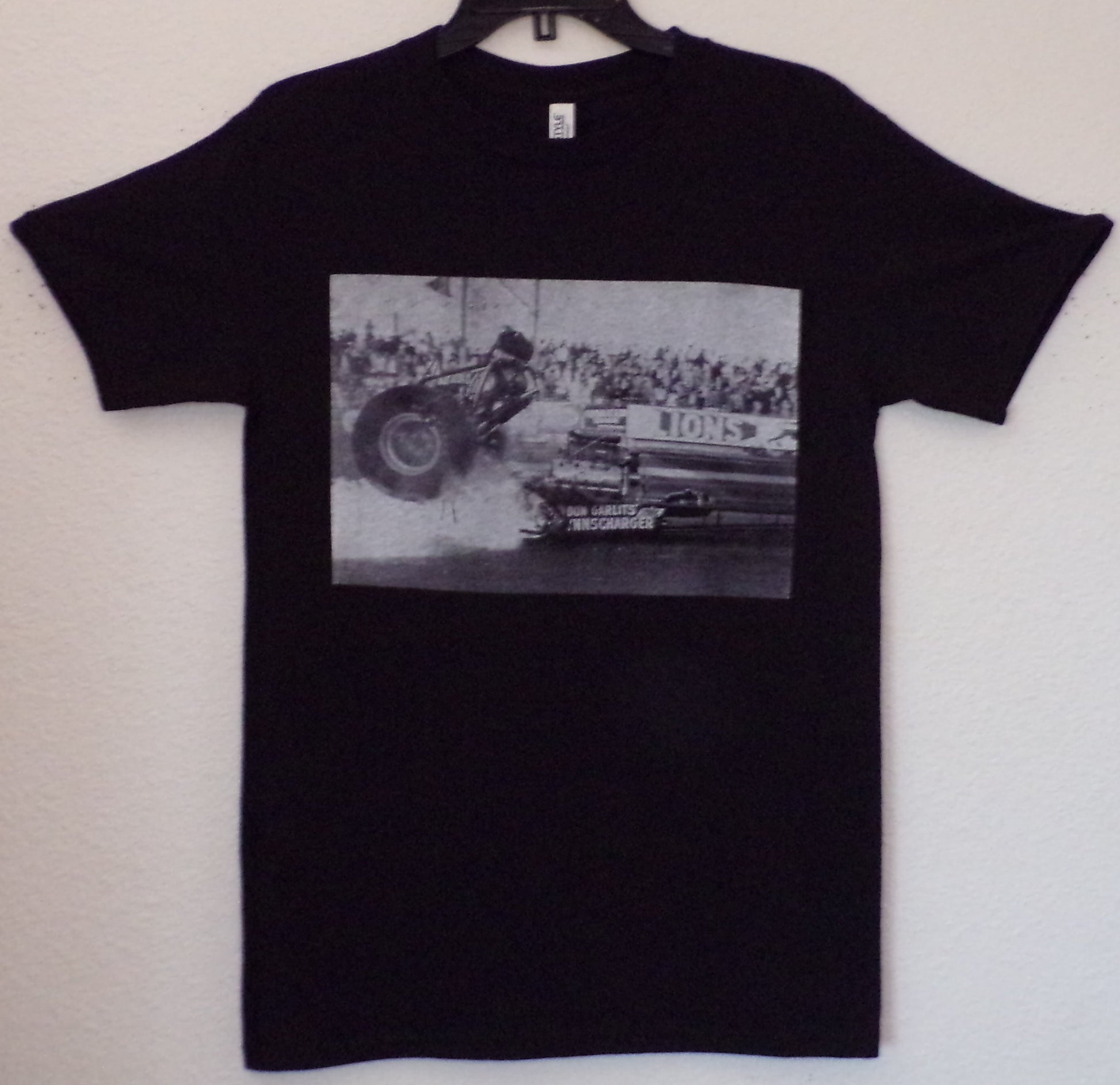 Black “Don Big Daddy Garlits – Clutch Explosion” unisex T-shirt featuring a historic black-and-white image from Lions Drag Strip, Small–3XL.