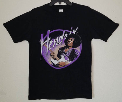 Black “Jimi Hendrix – Purple Haze” unisex T-shirt featuring Hendrix playing guitar with a vivid purple background design, Small–3XL.