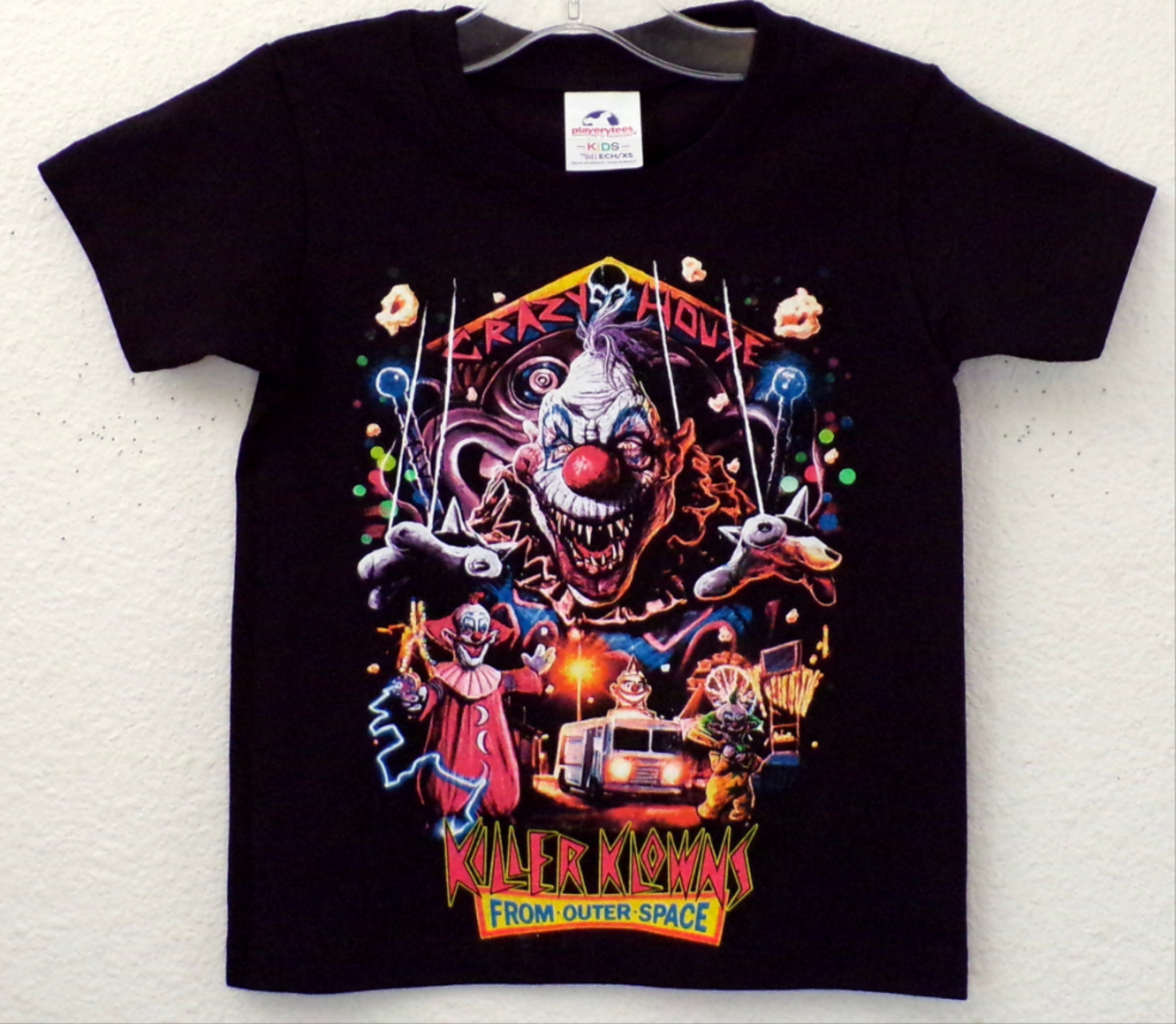  Youth-sized Killer Klowns From Outer Space - Crazy House horror t-shirt featuring a bold, colorful design inspired by the iconic 1980s horror film. The graphic showcases the eerie "Crazy House" theme, with a vibrant, creepy clown motif, making it a perfect choice for young horror fans. The shirt is shown in a close-up with clear visibility of the design on a soft, cotton fabric. Available in XS - XL.