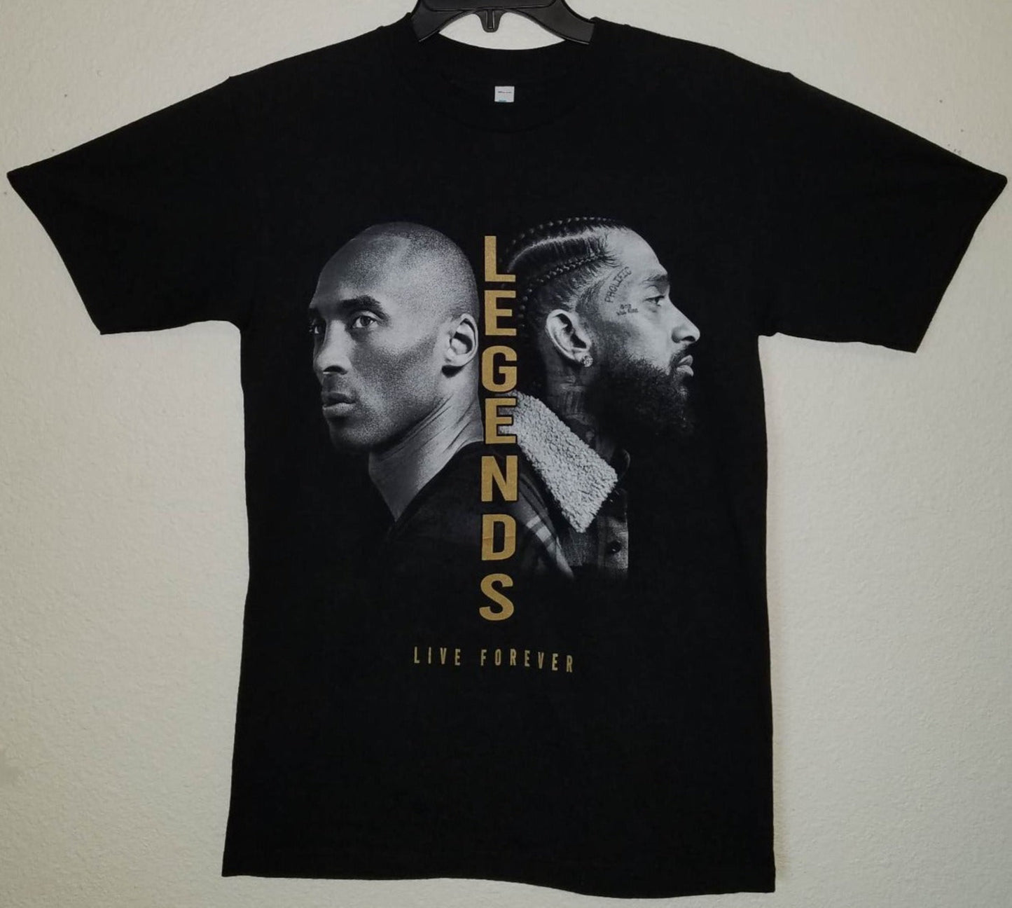 Front view of Kobe Bryant and Nipsey Hussle Legends Live Forever graphic T-shirt featuring black and white portraits with gold lettering printed in authentic silkscreen on black cotton tee