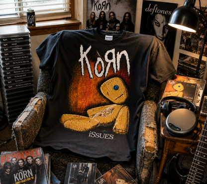 Korn Issues rag doll black T-shirt displayed in a music-filled bedroom setting—a nostalgic late-’90s nu metal shirt for Korn fans and collectors.
