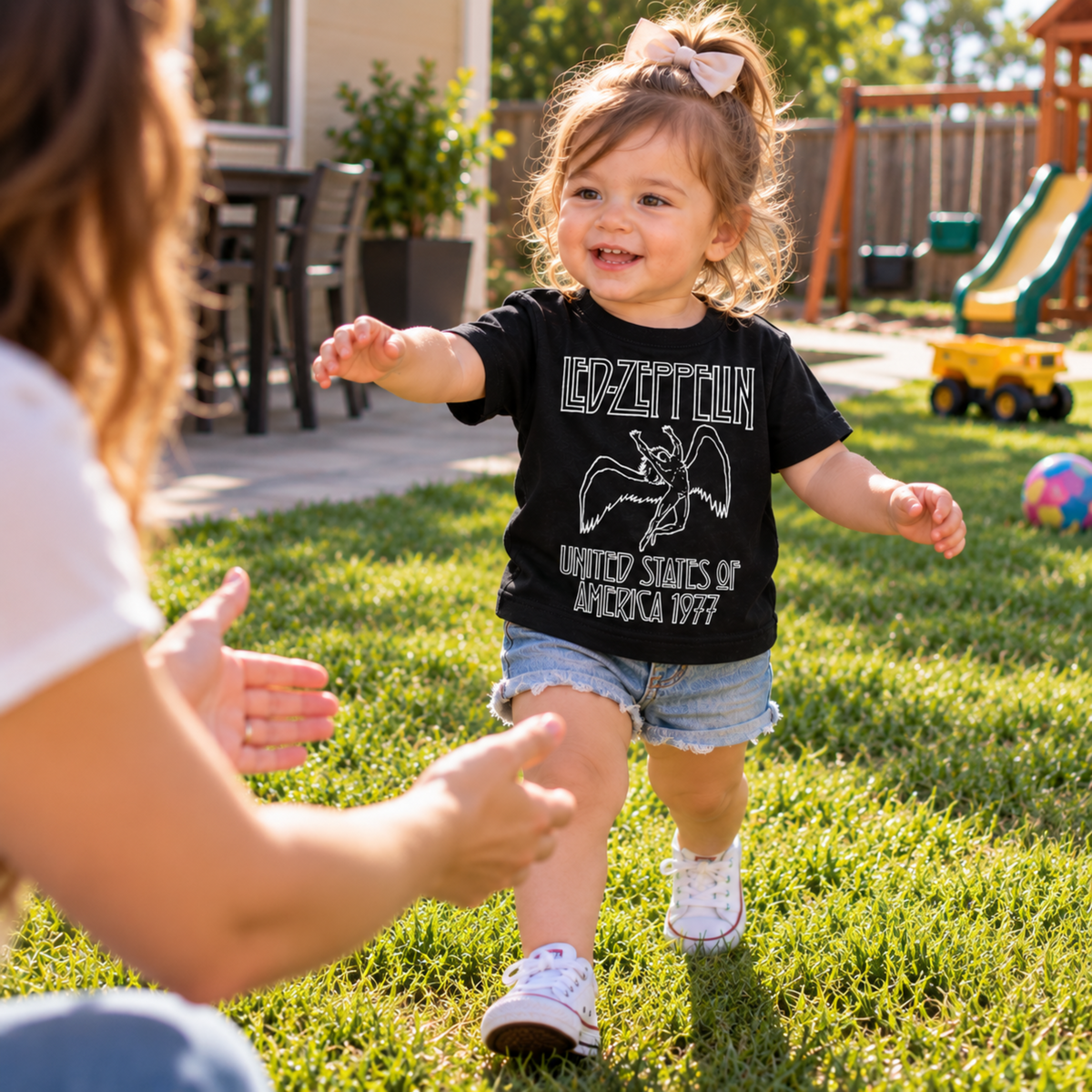 Child wearing a Led Zeppelin America 1977 black infant graphic T-shirt while walking outdoors.
