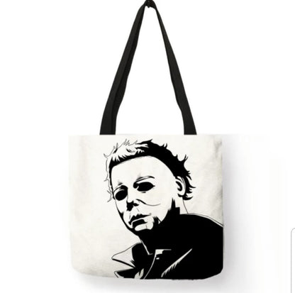 Cream off-white Michael Myers double-sided canvas tote bag with black handles, featuring a black-and-white portrait of the Halloween killer with his head tilted downward, dark eye sockets, messy hair, and shadowed clothing.