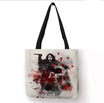 Cream off-white Scream Ghostface double-sided canvas tote bag with black handles, featuring the masked killer holding a knife amid red blood splatters and smoky gray horror artwork.