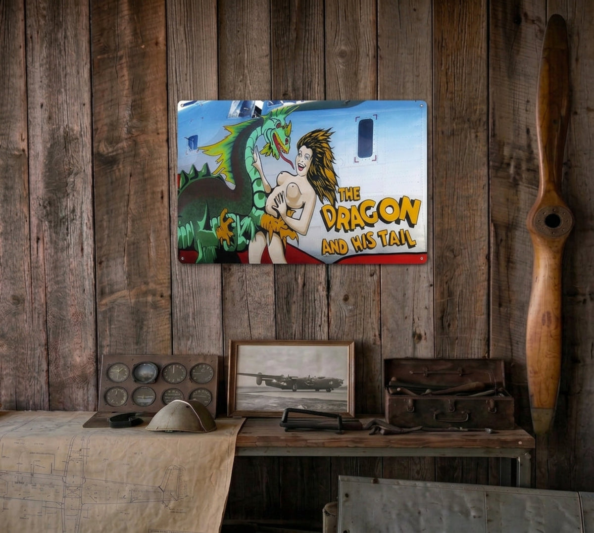 The Dragon and His Tail B-24J Liberator nose art sign displayed on a rustic wood wall above an aviation collector's cabinet.