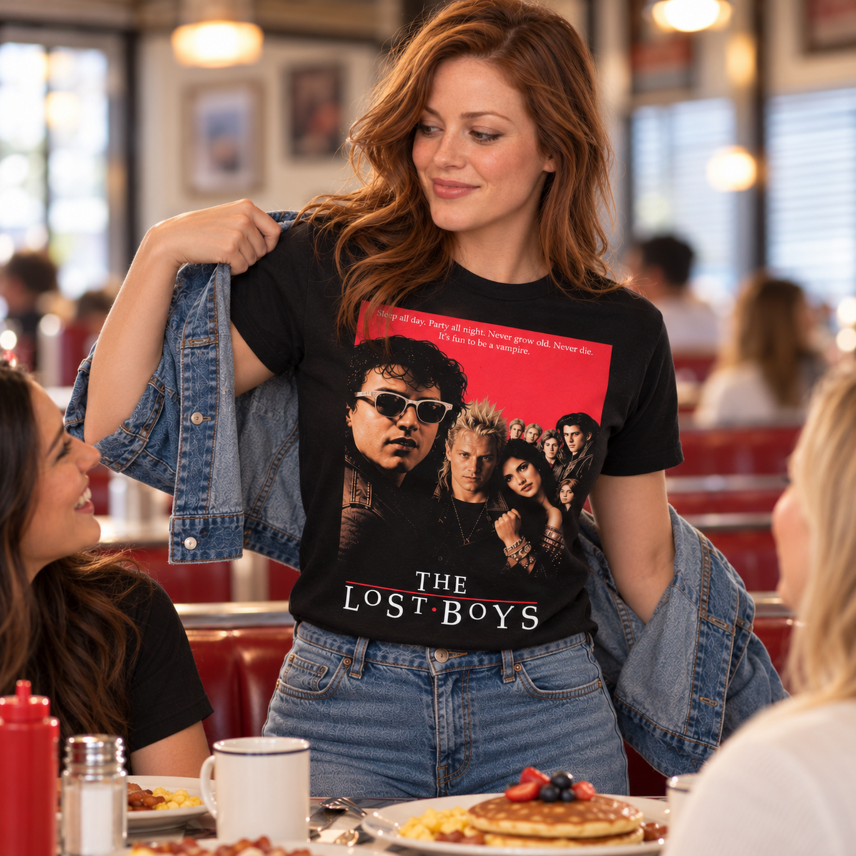 Woman wearing The Lost Boys black graphic T-shirt while having breakfast in a classic diner, featuring the original 1987 movie-cover cast artwork.