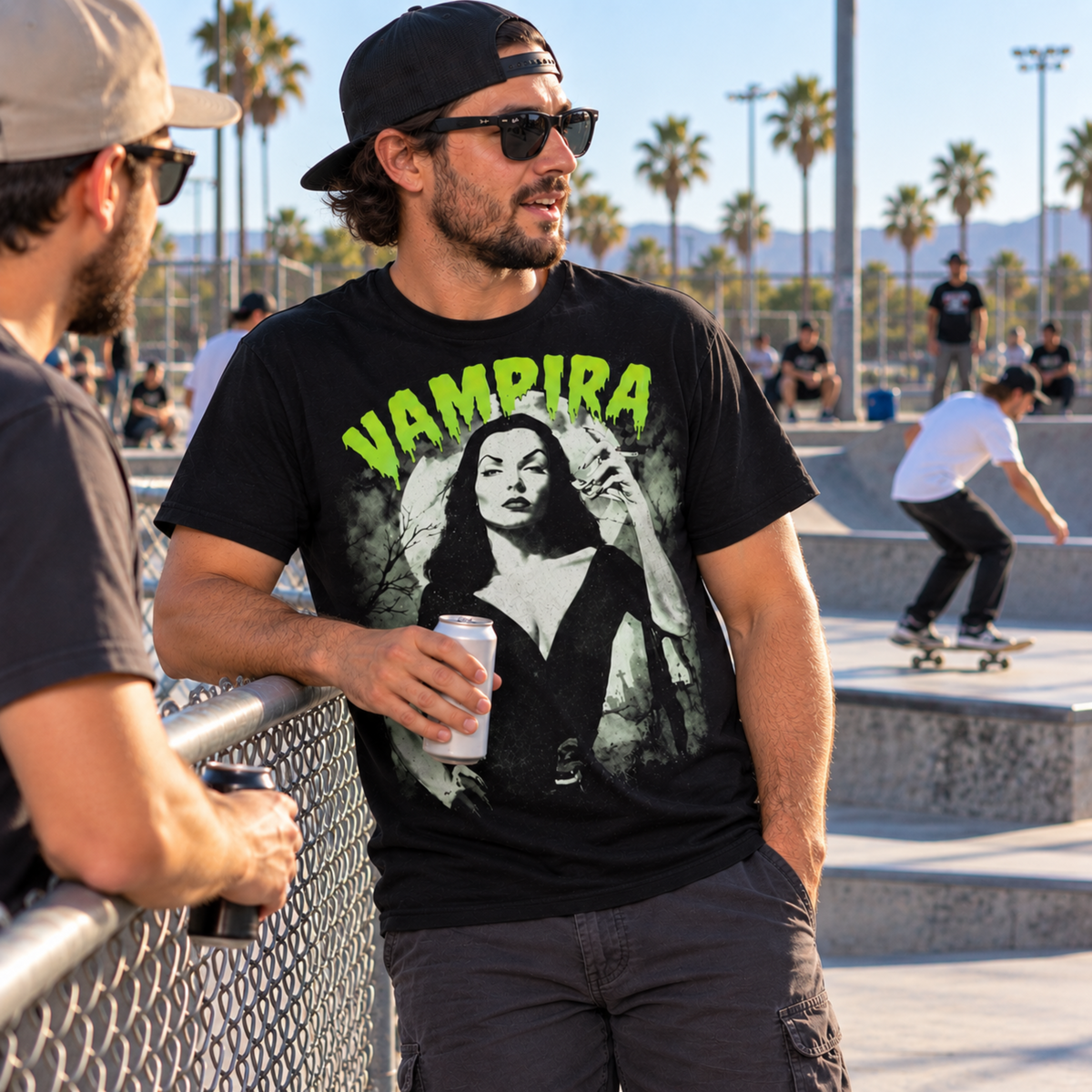 Man wearing the Vampira The Glamour Ghoul black T-shirt while hanging out with a friend at a skatepark, featuring her portrait and bright green VAMPIRA lettering.